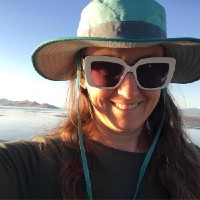 A selfie of Lara smiling at Great Salt Lake wearing a sunhat and dark sunglasses