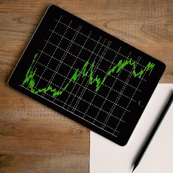 Tablet showing stock prices laying on table with pen and paper