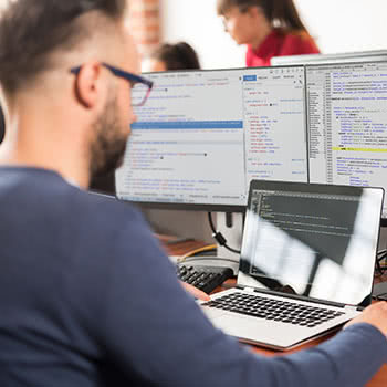 Man looks at code on laptop with dual-monitors
